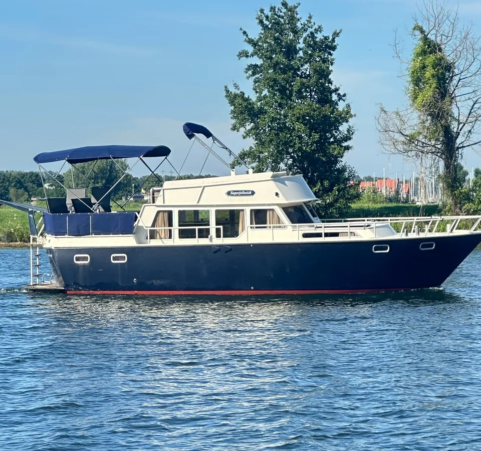 Een donkerblauwe motorboot met een crèmekleurige opbouw en een rood onderwaterschip vaart op een waterweg.