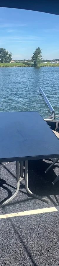 Een dek met een tafel en vier stoelen, met uitzicht op water en een groene oever.
