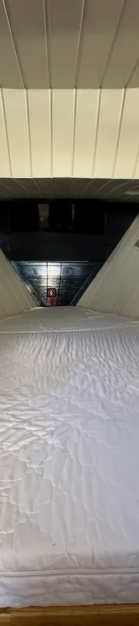 Een kajuit met een groot wit matras, twee patrijspoorten met gordijnen aan elke zijde en een licht plafond.
