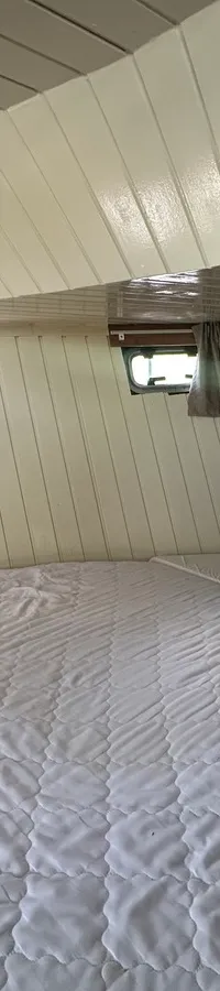 Een slaapkamer in een boot met een groot bed, twee kleine ramen met gordijnen en een televisie aan de muur.