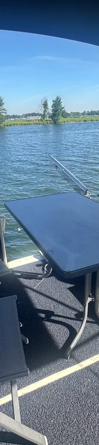 Een dek met vier donkere stoelen en een donkere tafel, met uitzicht op water en een groene oever.