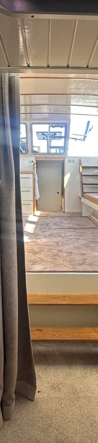 De foto toont het interieur van een boot met een doorkijk naar een andere ruimte, met planken, een gordijn en een…