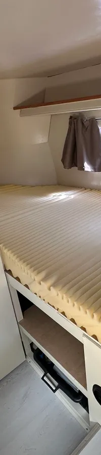 De foto toont een kajuit met een bed met een geribbeld matras, twee patrijspoorten en een witte kastdeur. — Oomen kruiser fly