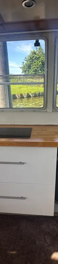 Een kombuis met een houten aanrechtblad, een spoelbak, een kookplaat, een koelkast en lades.