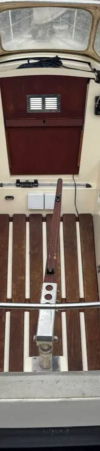 De foto toont het interieur van een kajuit met een houten tafel, twee banken met grijze kussens en houten wanden.
