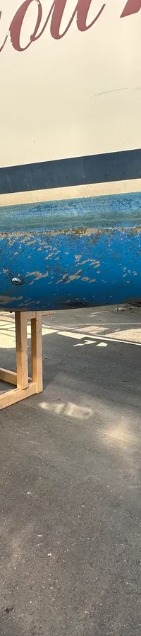 De foto toont de romp van een boot met een blauwe onderkant en een witte bovenkant, staand op een houten bok. — Compromis 777