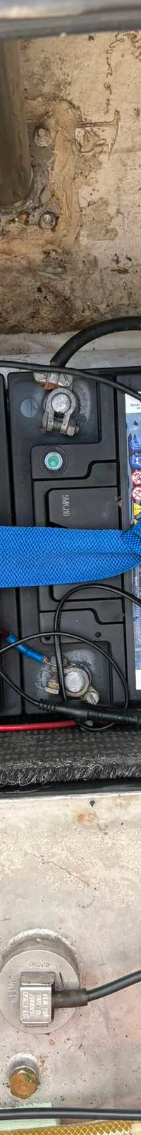 Vier zwarte accu's met blauwe banden en rode en zwarte kabels zijn zichtbaar boven een metalen tank.