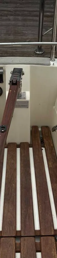 De foto toont het interieur van een boot met een zithoek, een kombuis met spoelbak en kookplaat, en houten kasten.