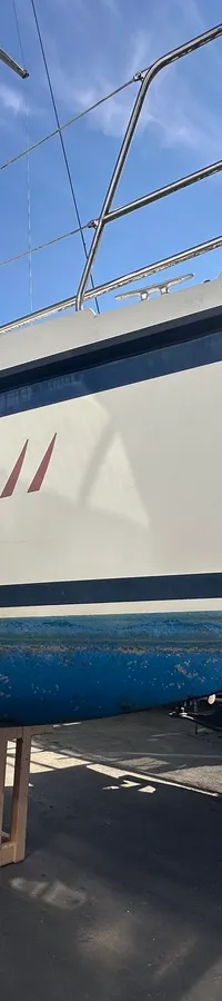 Een witte zeilboot met de naam "Bijou II" in rode letters staat op houten bokken naast een donkere boot. — Compromis 777