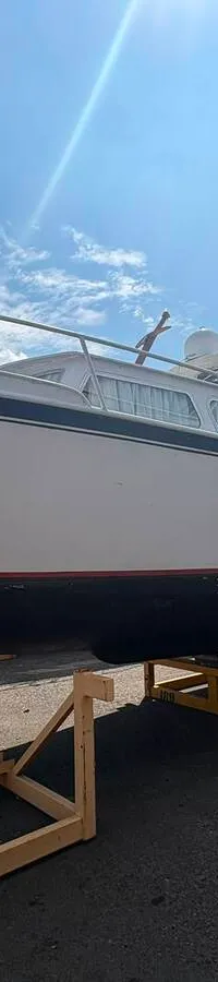 Een witte boot met de naam "Nino" op de boeg staat op een trailer op een buitenterrein onder een blauwe lucht.