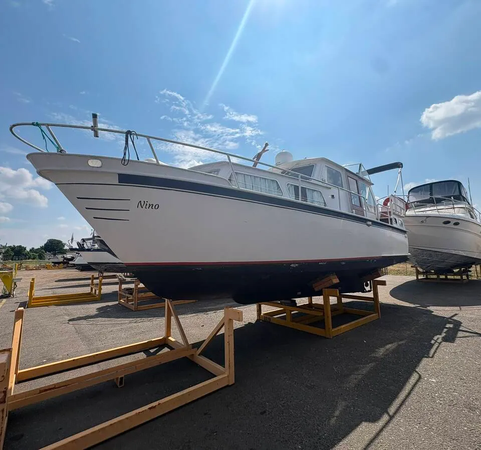 Een witte boot met de naam "Nino" op de boeg staat op een trailer op een buitenterrein onder een blauwe lucht.