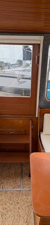De foto toont het interieur van een boot met een houten plafond, ramen met gordijnen, een televisie, een koelkast, een…