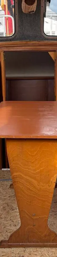 De foto toont het interieur van een boot met houten meubilair, witte kussens, een tafel en een witte stoel met blauwe biezen.