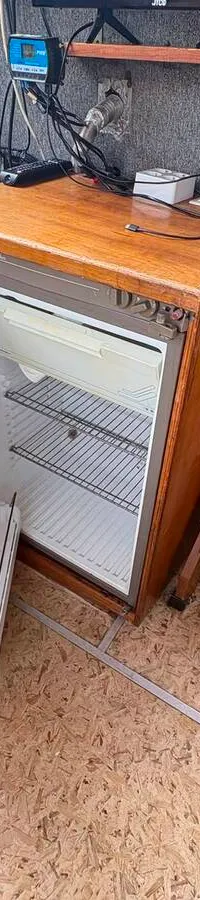 Een open koelkast is zichtbaar in een houten interieur met een tafel, banken, gordijnen en een trapje.
