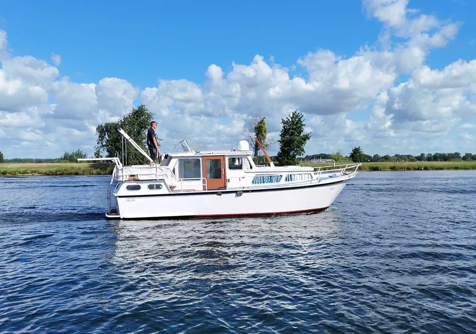 Een witte motorboot met een rode streep op de romp vaart op blauw water onder een bewolkte hemel. — Smelne 950 ak