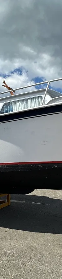 Een witte motorboot met de naam "Nino" op de boeg staat op een gele bok op een betonnen ondergrond onder een bewolkte hemel.