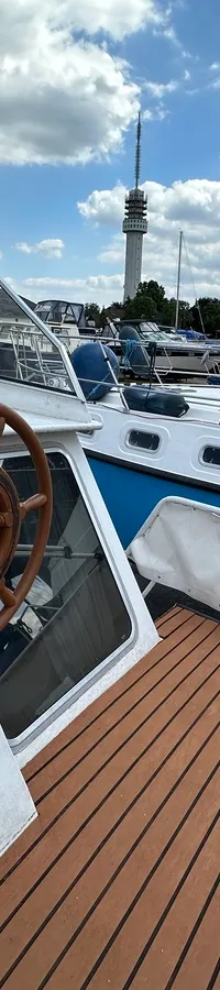 Een houten stuurwiel is zichtbaar op een bootdek met een bruine vloer en een Duitse vlag.