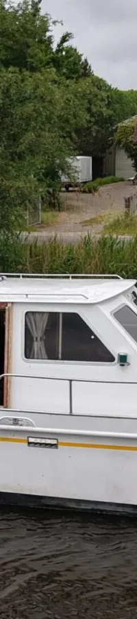Een witte motorboot met een gele streep vaart op het water, met een persoon in de kajuit en zonnepanelen op het dak.