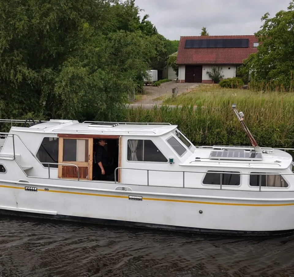 Een witte motorboot met een gele streep vaart op het water, met een persoon in de kajuit en zonnepanelen op het dak.