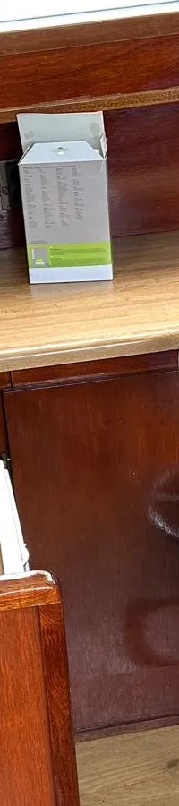 Een interieur van een boot met een fornuis, waterkoker, boiler, blauwe bureaustoel en een bankje met maritieme kussens.