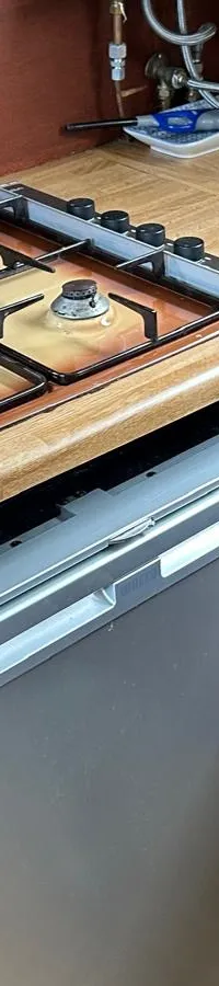 Een kombuis met een gasfornuis met vier pitten, een waterkoker, een koelkast en een blauwe bureaustoel.
