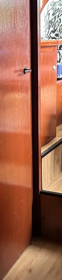 Een houten interieur met een open deur naar een andere ruimte en een bed met een groen kussen op de voorgrond.