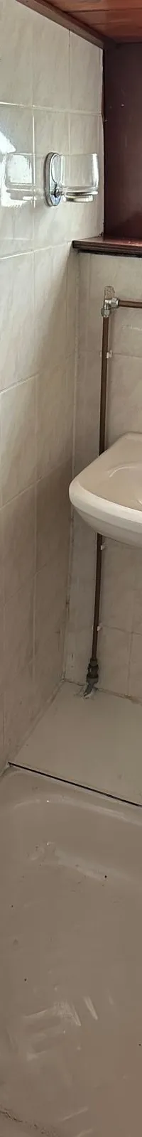 Een badkamer met een wastafel, douche en een douchegordijn, met tegels op de wanden en een raam.