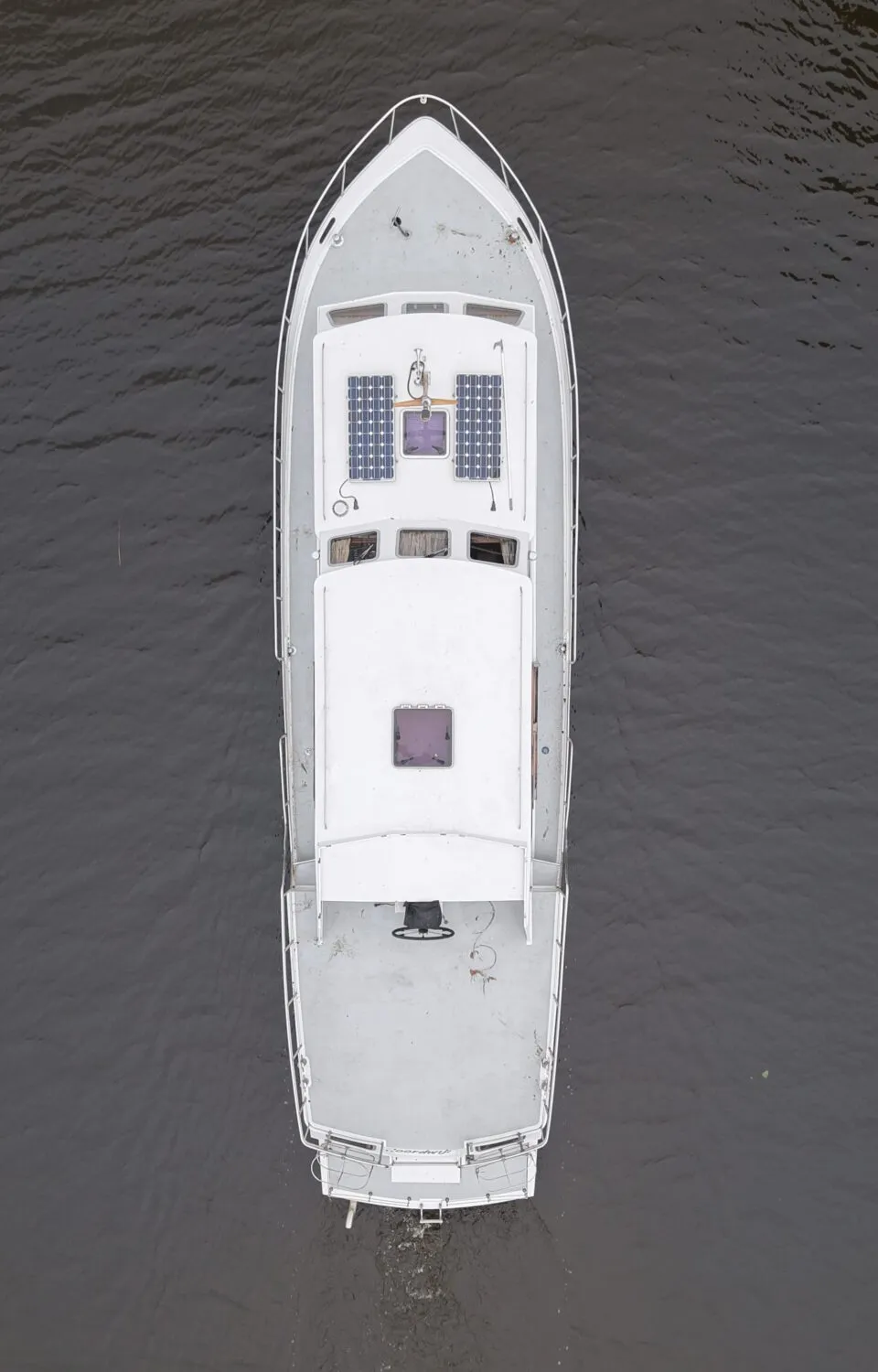 Een wit motorjacht met zonnepanelen op het dak vaart op een donker waterkanaal omzoomd met groen riet.