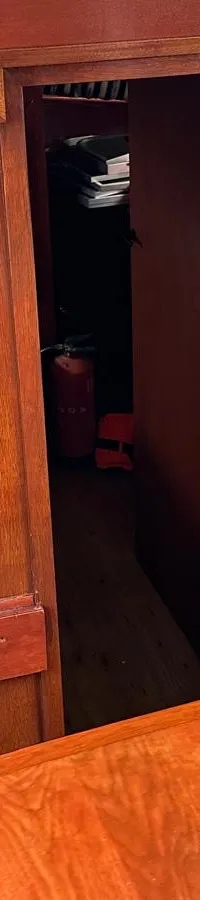 De foto toont een houten interieur van een boot met blauw-wit gestreepte gordijnen en kussens met nautische patronen.