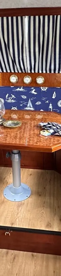 Een interieur van een boot met een blauwe hoekbank met nautische print, een houten tafel, een blauwe bureaustoel en…