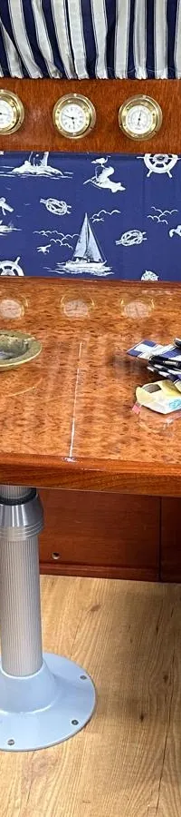 Een kajuit met een houten tafel, blauwe banken met nautische patronen en een blauwe stoel.