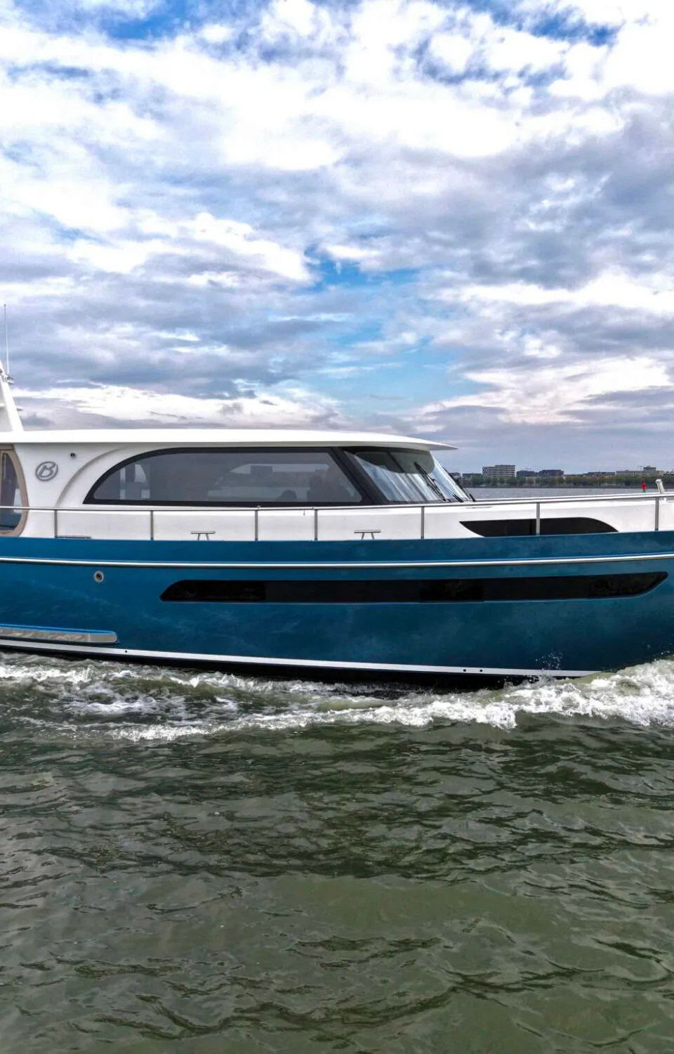 Een blauw-witte motorboot vaart op het water, met een stad aan de horizon onder een bewolkte lucht.