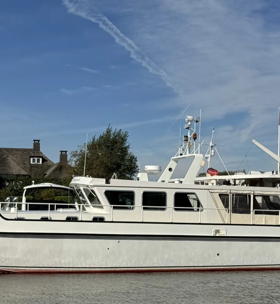 Een witte motorboot met de naam "M.S. Compagnon" ligt in het water, met een rode onderkant en zwarte stootrand.