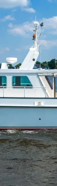 Een witte motorboot met een rode waterlijn vaart op een waterweg met huizen en bomen op de achtergrond.