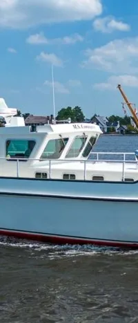 Een witte motorboot met de naam "M.S. Compagnon" vaart op een waterweg met huizen en bomen op de achtergrond.