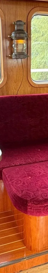 Een interieur van een boot met houten wanden, een rode bank, een tafel en ramen met uitzicht op water en bomen.