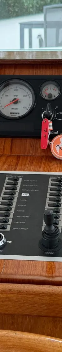 Een houten dashboard van een boot met diverse meters, schakelaars, een marifoon en een gashendel.