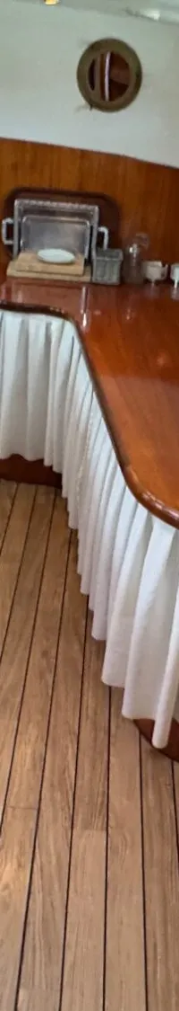 Een interieur van een boot met een houten vloer, een kombuis met aanrecht en een bar, en ramen met houten kozijnen.