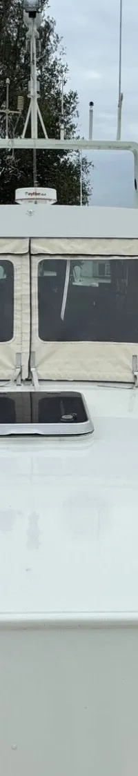 De foto toont het voordek van een witte boot met een beige cabriokap en een luik in het midden.