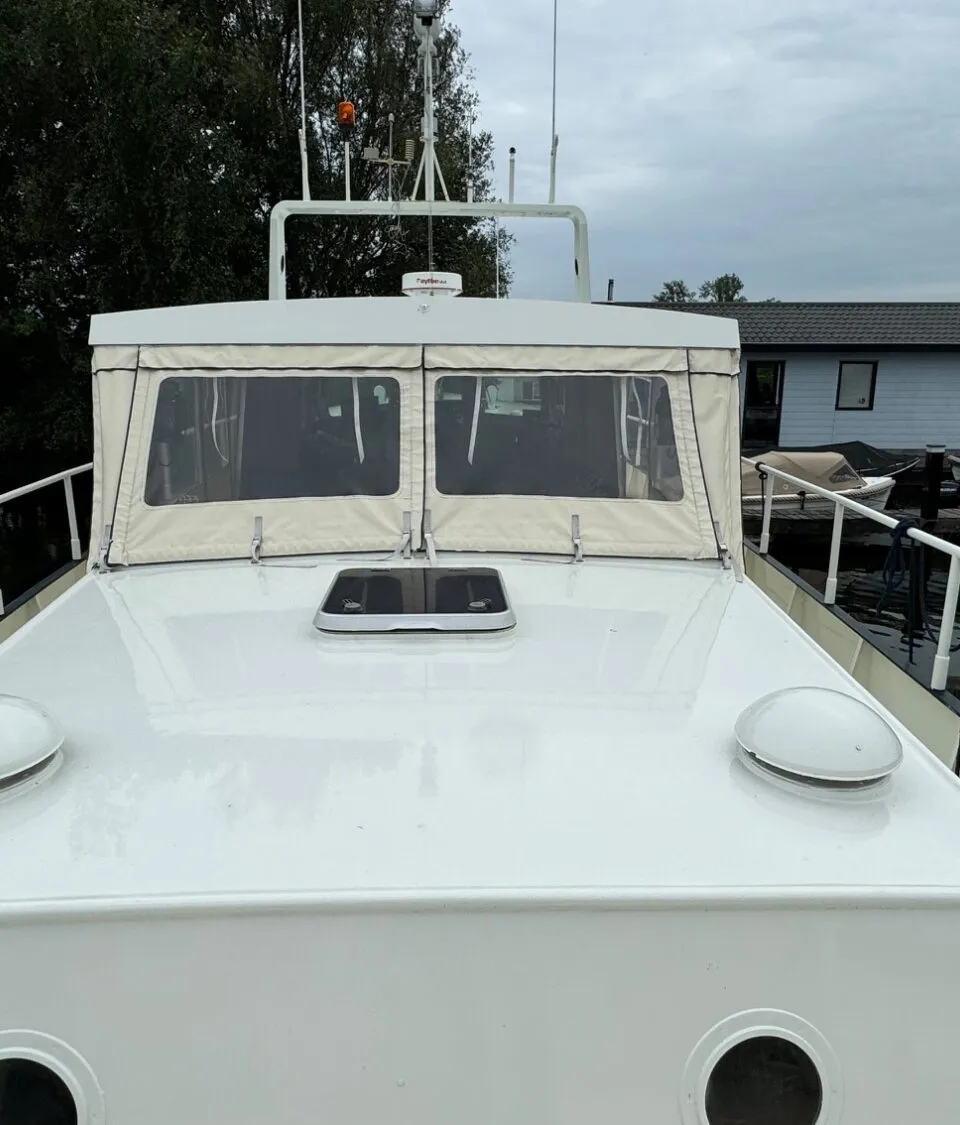 De foto toont het voordek van een witte boot met een beige cabriokap en een luik in het midden.