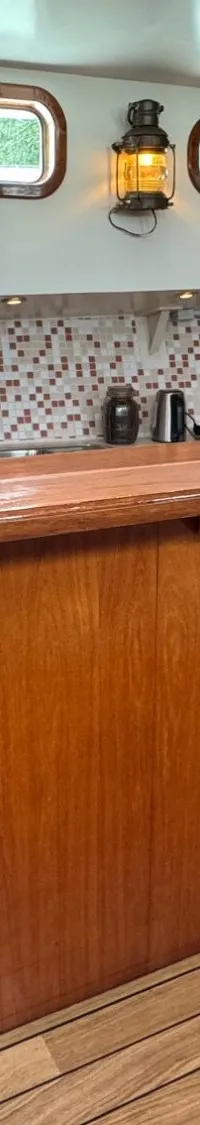 Een interieur van een boot met een houten bar, een tapkraan, een gootsteen, een magnetron en een koelkast.
