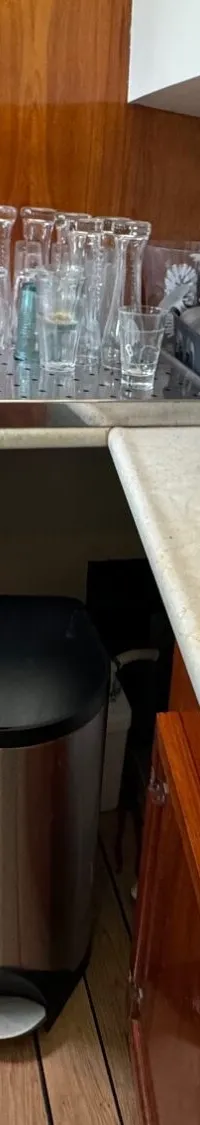 Een kombuis met een dubbele spoelbak, een kraan, een biertap, glazen, een koelkast en een prullenbak.