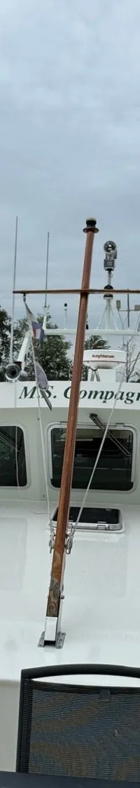 Een witte boot met de naam "M.S. Compagnon" ligt in het water, met andere boten en huizen op de achtergrond.