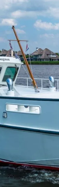 Een witte motorboot met de naam "M.S. Compagnon" vaart op een waterweg met huizen en bomen op de achtergrond.