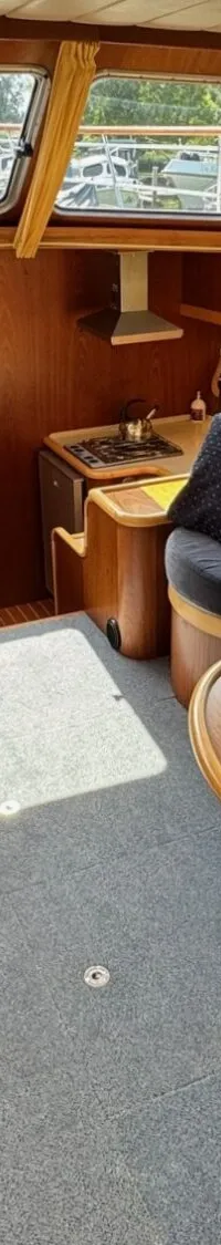De foto toont het interieur van een boot met houten wanden, twee banken met donkerblauwe kussens en een ovale tafel.