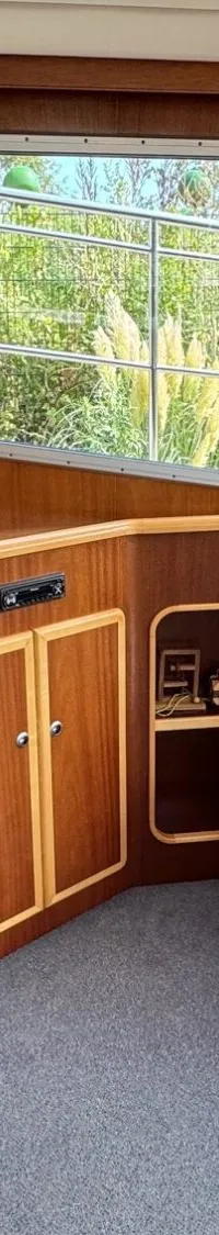 Een interieur van een boot met houten lambrisering, een trap, een bank met kussens en ramen met gordijnen.