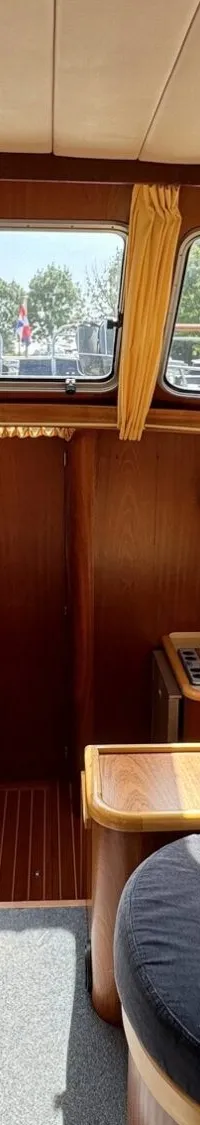 De foto toont het interieur van een boot met houten afwerking, zitbanken, een tafel en een kleine keuken.