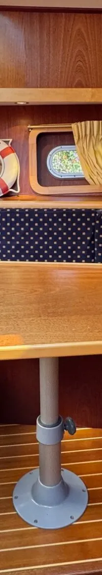 Een houten interieur van een boot met een U-vormige bank met blauwe kussens en een houten tafel in het midden.