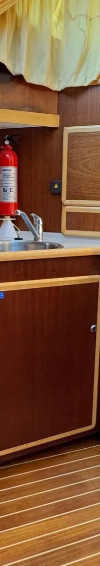Een kombuis met houten kasten, een fornuis, een spoelbak, een koelkast en een brandblusser.