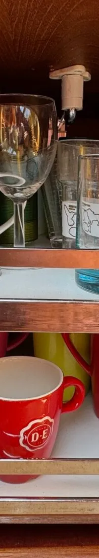 Een open kastje met twee draaiplateaus vol glazen en mokken, naast een paneel met schakelaars.